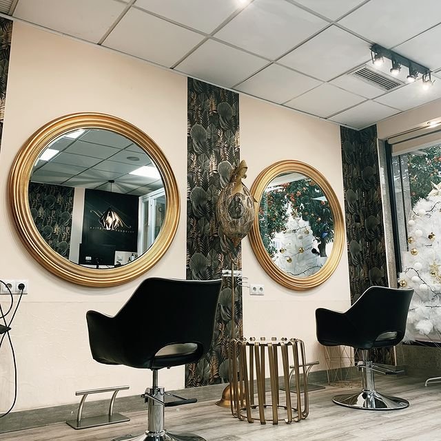 Interior de la peluquería con dos sillas negras frente a espejos circulares dorados, decorado con un árbol de Navidad blanco.